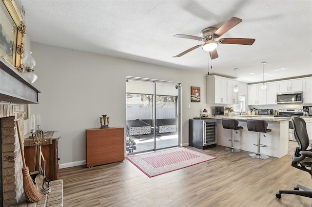 living room featuring a ceiling fan, light wood-style floors, baseboards, a brick fireplace, and wine cooler