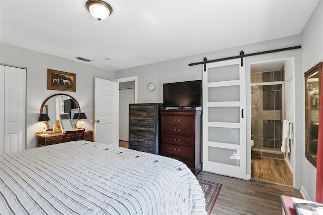 bedroom featuring a barn door, wood finished floors, visible vents, a closet, and ensuite bath