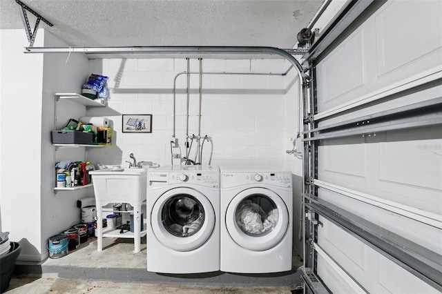 washroom with laundry area, concrete block wall, a sink, washer and dryer, and a textured ceiling