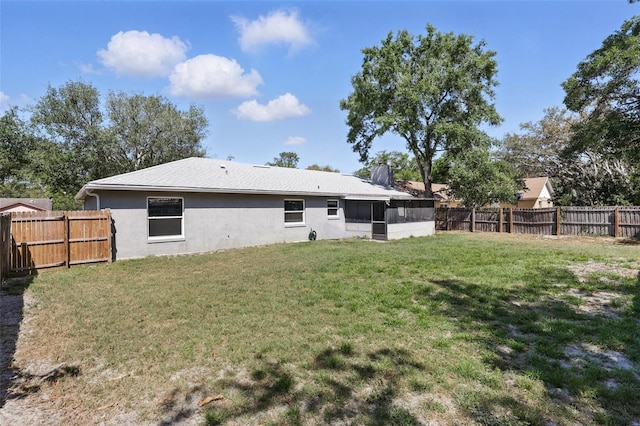 rear view of property with a fenced backyard, a sunroom, a yard, and stucco siding