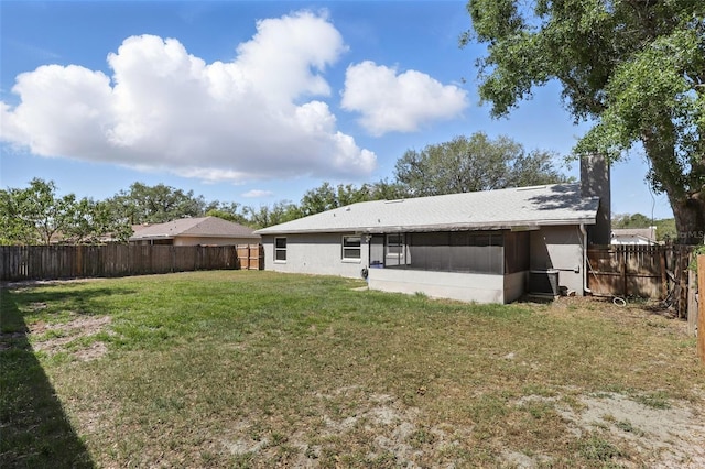 back of property with a sunroom, a lawn, a chimney, and a fenced backyard