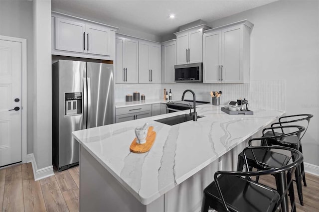 kitchen with tasteful backsplash, a peninsula, light stone countertops, appliances with stainless steel finishes, and a sink