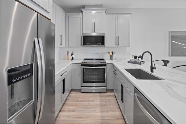kitchen featuring a sink, light wood-style floors, stainless steel appliances, decorative backsplash, and light stone counters