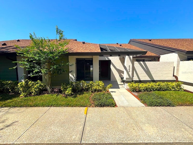 view of front of property with roof mounted solar panels, a shingled roof, and stucco siding