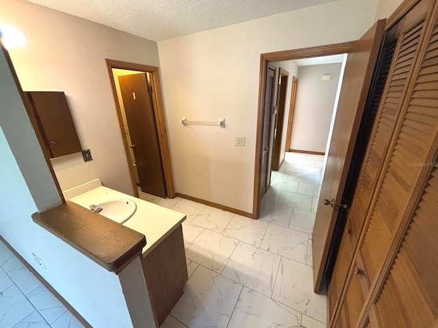 bathroom featuring a textured ceiling, marble finish floor, baseboards, and a sink