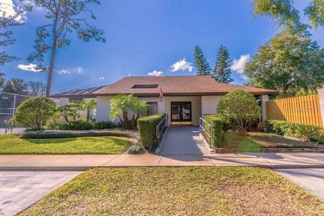 ranch-style house with stucco siding, a front lawn, fence, and solar panels