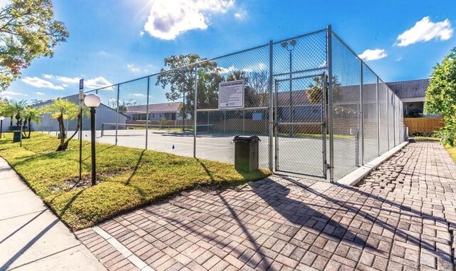 view of property's community with a gate, a tennis court, and fence