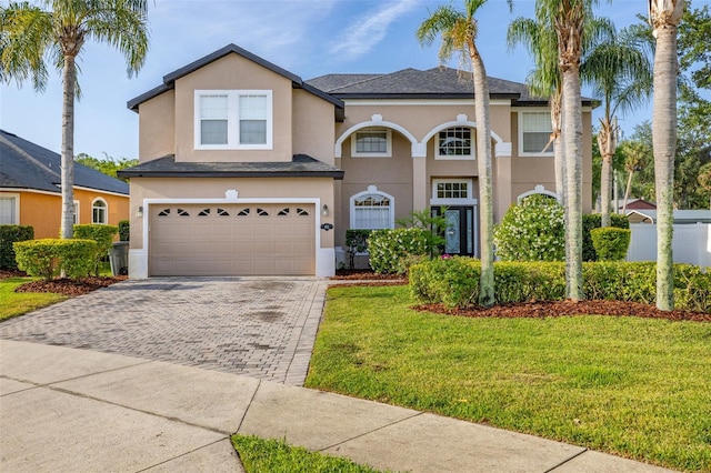 traditional-style house with decorative driveway, a front lawn, and stucco siding