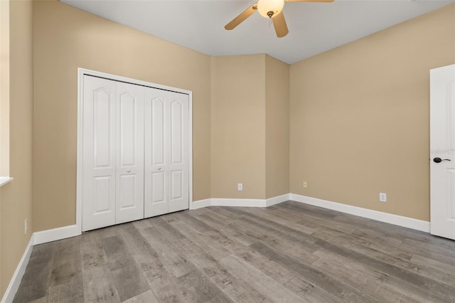 unfurnished bedroom featuring baseboards, a ceiling fan, wood finished floors, and a closet