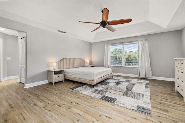 bedroom with a raised ceiling, baseboards, wood finished floors, and visible vents