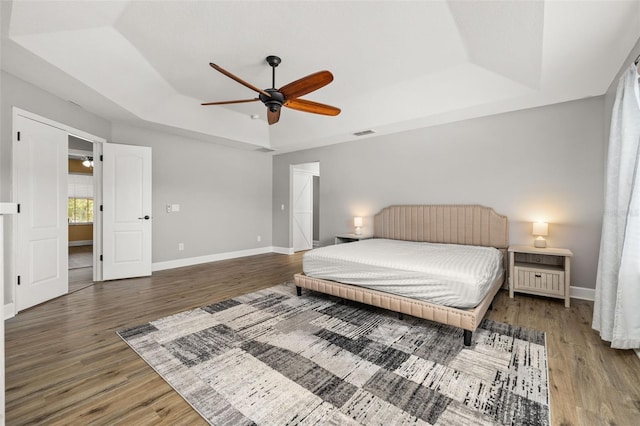bedroom with a tray ceiling, wood finished floors, and visible vents