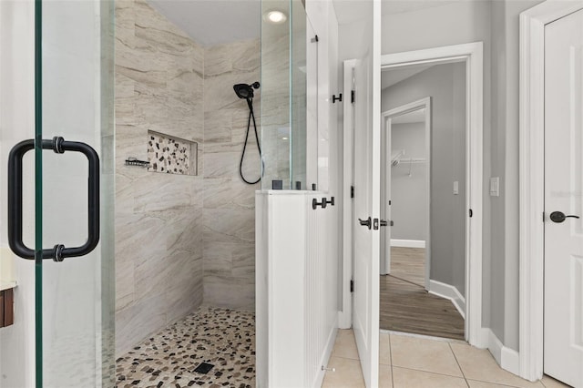 full bathroom featuring tile patterned flooring, baseboards, a stall shower, and a spacious closet