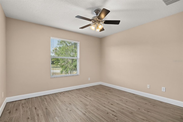 empty room with ceiling fan, a textured ceiling, visible vents, wood finished floors, and baseboards