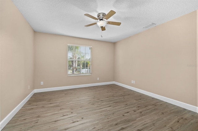 empty room featuring a textured ceiling, a ceiling fan, baseboards, wood finished floors, and visible vents
