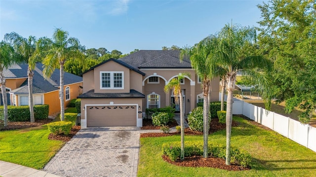 traditional home with a front lawn, fence, decorative driveway, stucco siding, and an attached garage