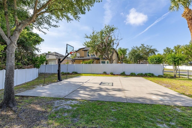 view of basketball court featuring a lawn, fence, and basketball hoop