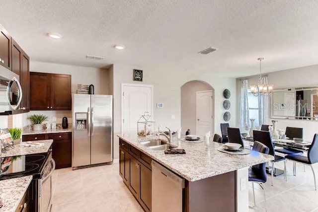 kitchen with a notable chandelier, a center island with sink, appliances with stainless steel finishes, arched walkways, and a sink