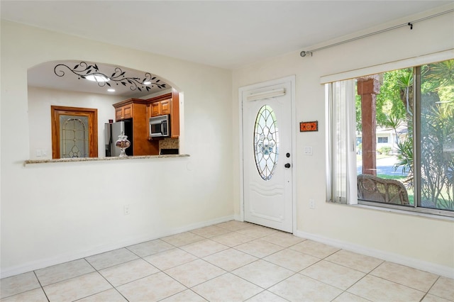foyer entrance with light tile patterned floors, arched walkways, and baseboards