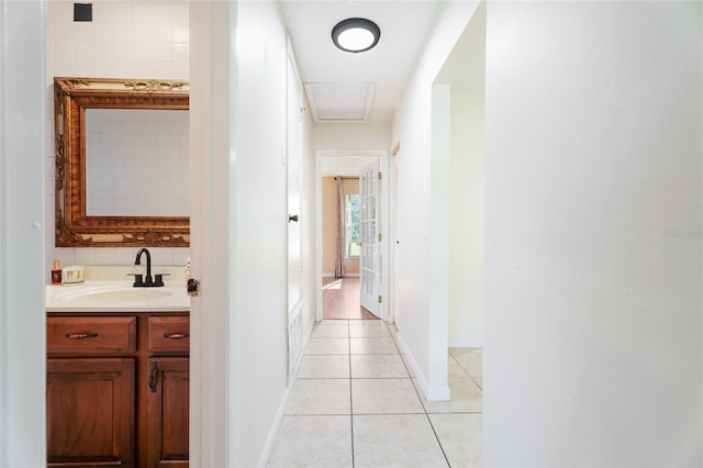 corridor with baseboards, a sink, and light tile patterned floors