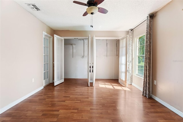 unfurnished bedroom featuring french doors, a textured ceiling, visible vents, wood finished floors, and two closets