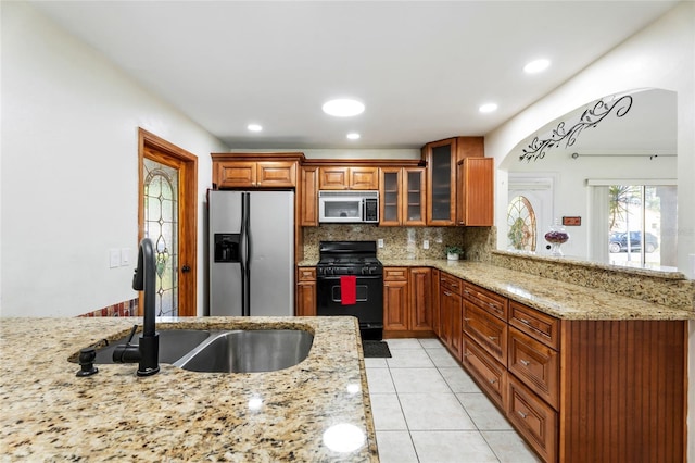 kitchen featuring backsplash, appliances with stainless steel finishes, light stone countertops, a sink, and glass insert cabinets