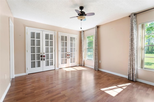 empty room with a ceiling fan, a textured ceiling, french doors, and wood finished floors