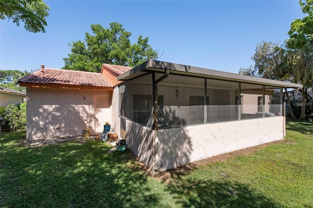 back of property featuring a yard, a tile roof, a sunroom, and stucco siding