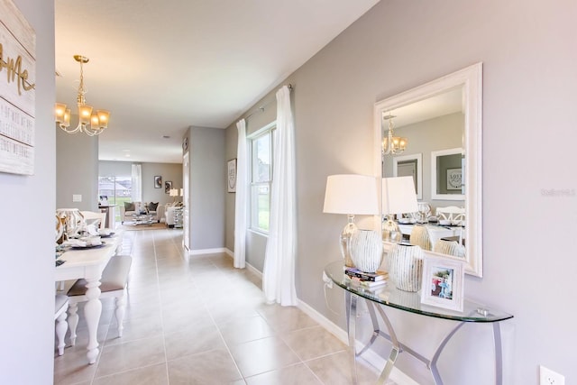 hallway with tile patterned floors, a chandelier, and baseboards