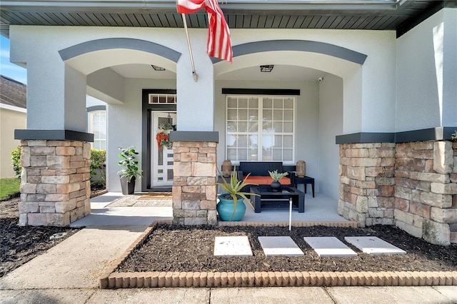 view of exterior entry with stucco siding, a porch, and stone siding