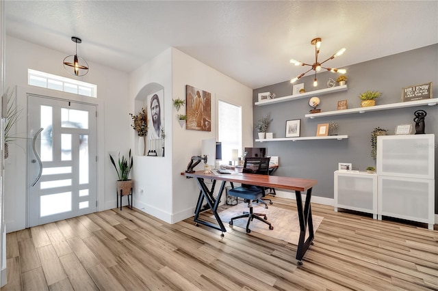 office area with light wood-type flooring, plenty of natural light, a notable chandelier, and arched walkways
