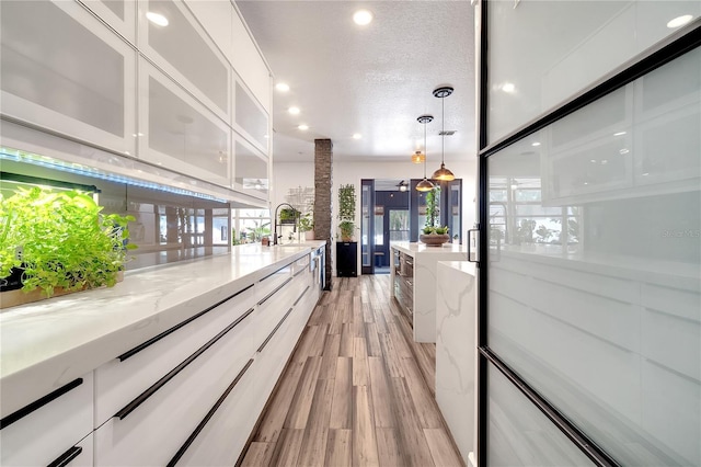 hallway with recessed lighting, a textured ceiling, light wood finished floors, and a sink