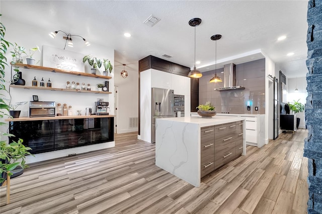 kitchen with light wood-style floors, visible vents, stainless steel refrigerator with ice dispenser, and wall chimney exhaust hood