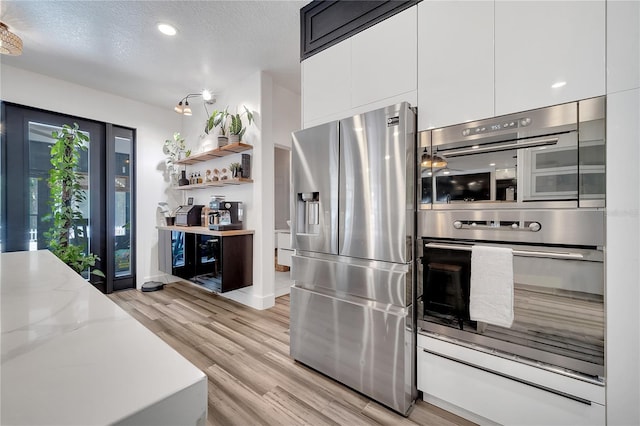 kitchen with light stone countertops, modern cabinets, light wood-style flooring, white cabinets, and appliances with stainless steel finishes