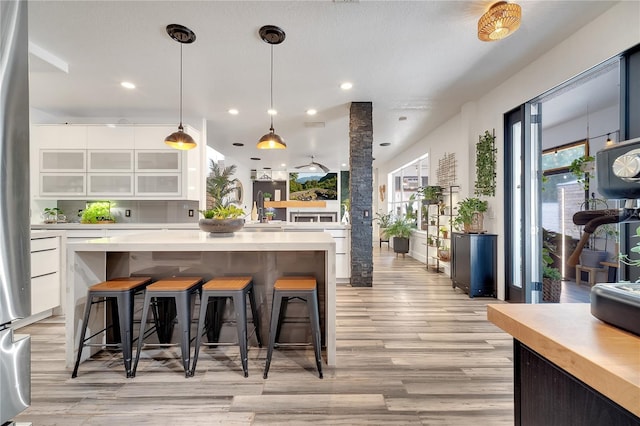 kitchen with light wood-type flooring, a center island, a breakfast bar, white cabinetry, and light countertops