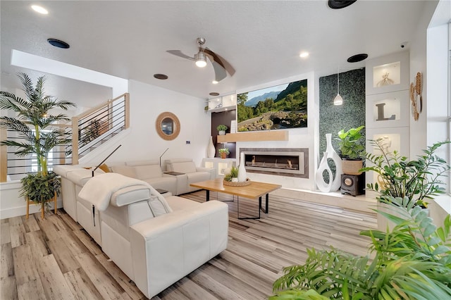 living room with light wood-type flooring, a ceiling fan, and a fireplace