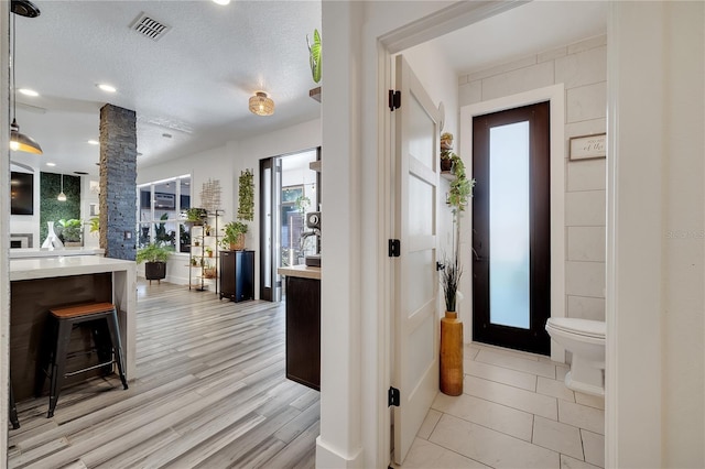 interior space featuring a textured ceiling, visible vents, toilet, decorative columns, and wood finished floors