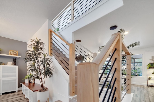 stairs with wood finished floors, a ceiling fan, and baseboards