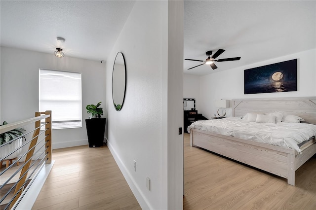 bedroom featuring a textured ceiling, light wood-style floors, ceiling fan, and baseboards