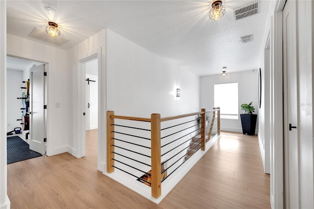 corridor with baseboards, visible vents, light wood-type flooring, and an upstairs landing