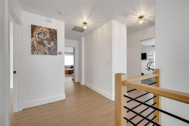 corridor featuring light wood-style floors, baseboards, visible vents, and an upstairs landing