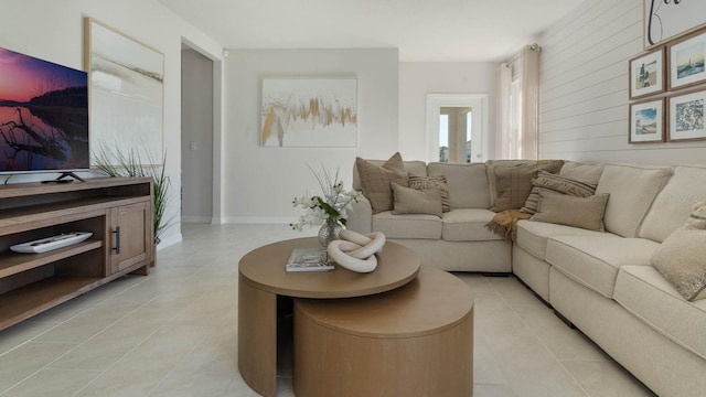 living room featuring wooden walls, baseboards, and light tile patterned flooring