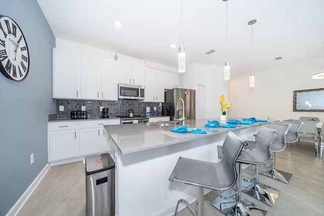 kitchen with an island with sink, tasteful backsplash, white cabinetry, a breakfast bar, and stainless steel appliances
