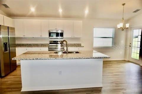 2607 Tulip Dr, Davenport, FL 33837 - kitchen featuring light stone counters, a chandelier, white cabinetry, appliances with stainless steel finishes, and wood finished floors