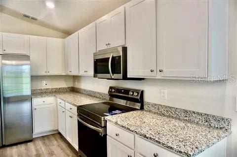 2607 Tulip Dr, Davenport, FL 33837 - kitchen with stainless steel appliances, light stone countertops, white cabinetry, and vaulted ceiling