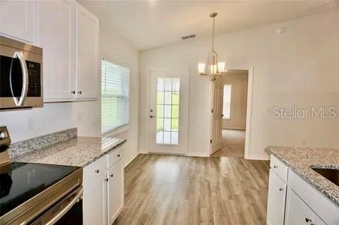 2607 Tulip Dr, Davenport, FL 33837 - kitchen with an inviting chandelier, plenty of natural light, light wood-style flooring, white cabinetry, and stainless steel appliances