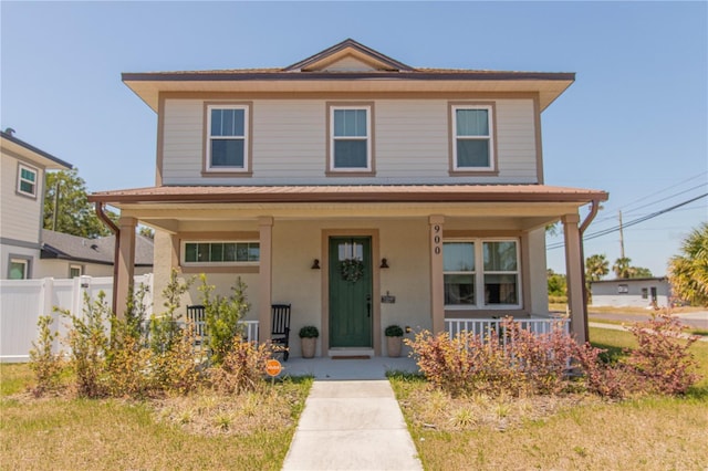 traditional style home featuring fence, covered porch, and stucco siding