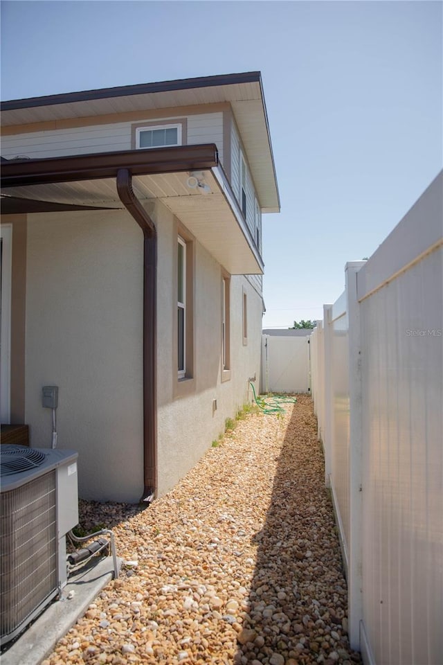 view of side of home with cooling unit, a fenced backyard, and stucco siding