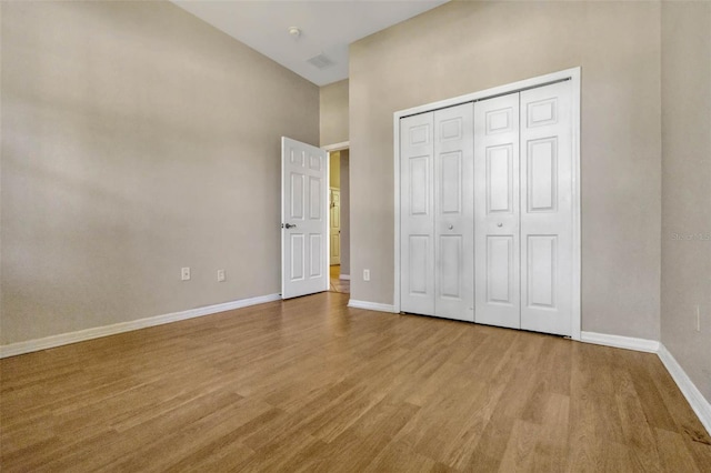 unfurnished bedroom featuring baseboards, wood finished floors, visible vents, and a closet