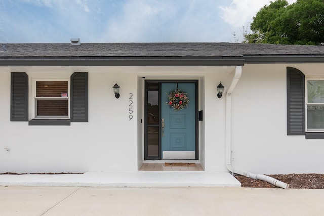 entrance to property featuring a shingled roof and stucco siding