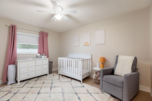 bedroom with light tile patterned floors, ceiling fan, a crib, and baseboards